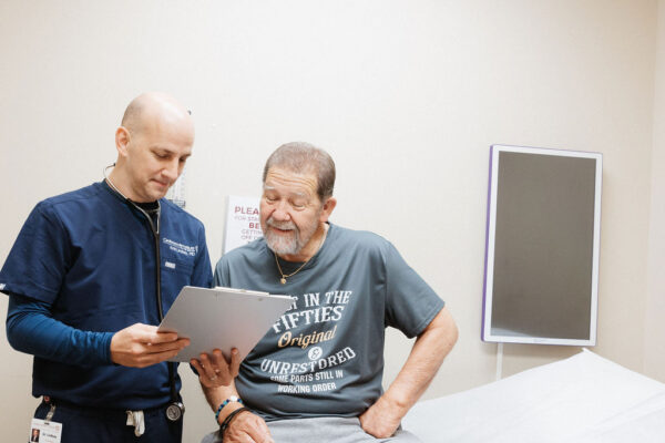 Kris Lindsay, MD, Cardiologist in New Iberia, Telecardiology, reviews a chart with a patient in an exam room