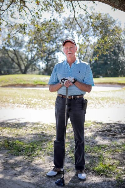 A confident golfer stands with a club in hand on a sunny day, ready for a round on the course, undeterred by his venous disease.