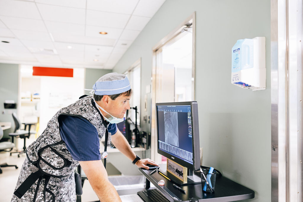 A doctor in a PPE gown examines a CT scan of a heart for Coronary Artery Disease