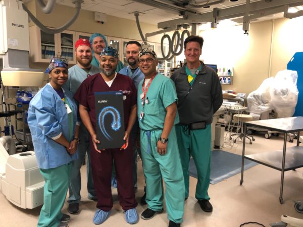 A group of happy looking CIS staff poses with a box containing the Eluvia stent