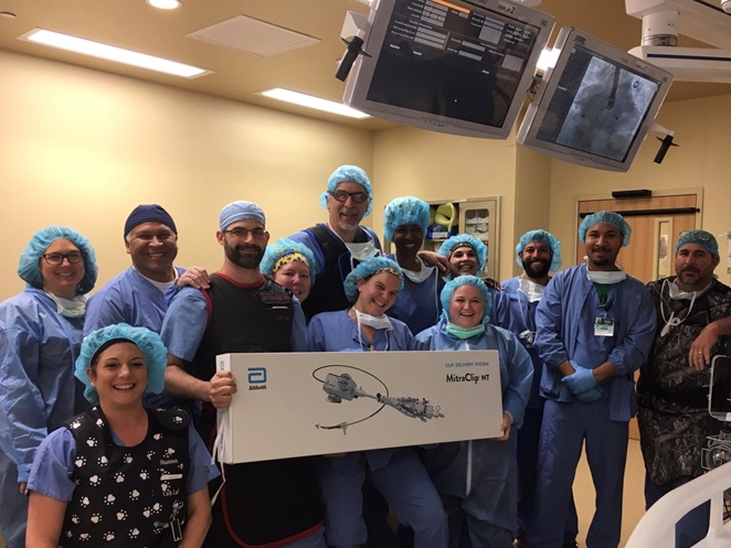 A smiling group of CIS staff members poses with a box containing the MitraClip® valve replacement device