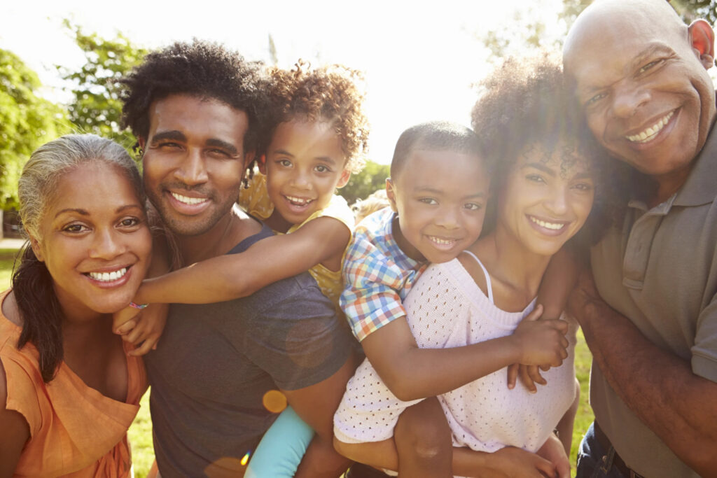 A joyful multi-generational family enjoying a sunny day outdoors, with warm smiles and embracing each other in a group hug, radiating heart health.