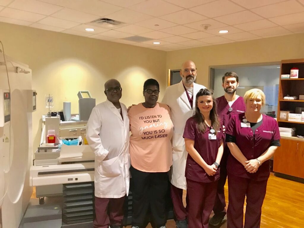 A group of CIS staff standing next to a cardiac positron emission tomography (PET) machine in an exam room