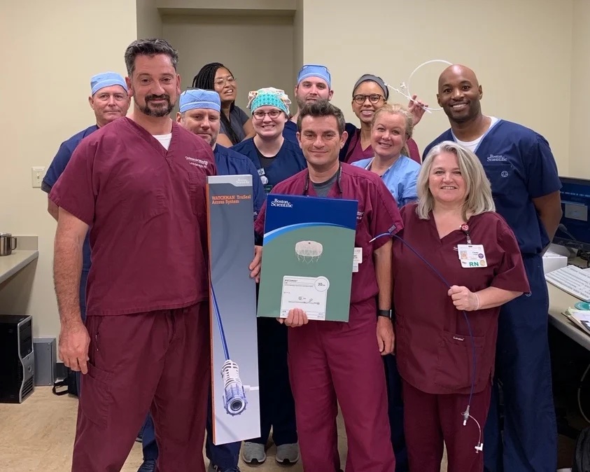 A smiling group of CIS staff members pose with boxes containing the components for the Watchman implant device