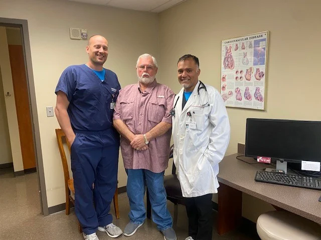 Three healthcare professionals posing for a photo in a clinic office, with anatomy posters in the background.