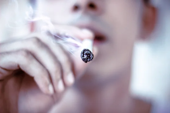 Close-up of an unidentifiable person smoking a cigar, with smoke curling around the glowing ember, highlighting concerns for those with Venous Disease.