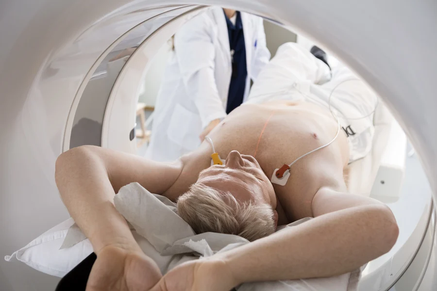 A patient lies inside a CT scanner for a heart health imaging procedure while a cardiologist assists.