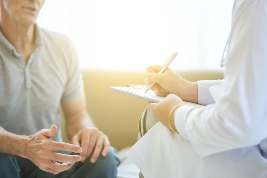 A cardiologist taking notes while consulting with an elderly patient in a bright, sunlit room.