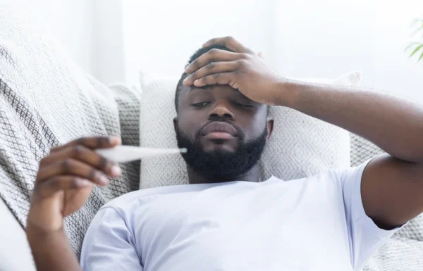 A man checking his temperature with a thermometer while looking unwell and holding his forehead, possibly concerned about his heart health.