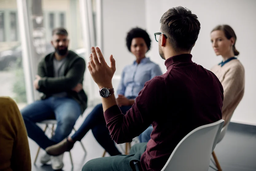 A cardiologist gesturing while speaking in a group discussion with attentive listeners in the background.