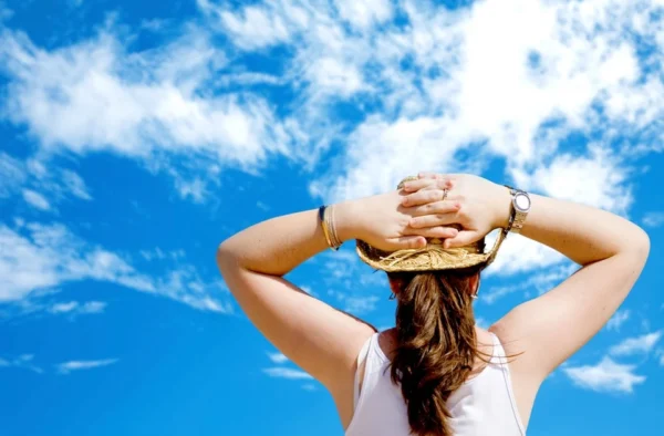 Relaxing under the blue sky: a cardiologist enjoys a sunny day, resting with her hands behind her head against a backdrop of fluffy clouds.