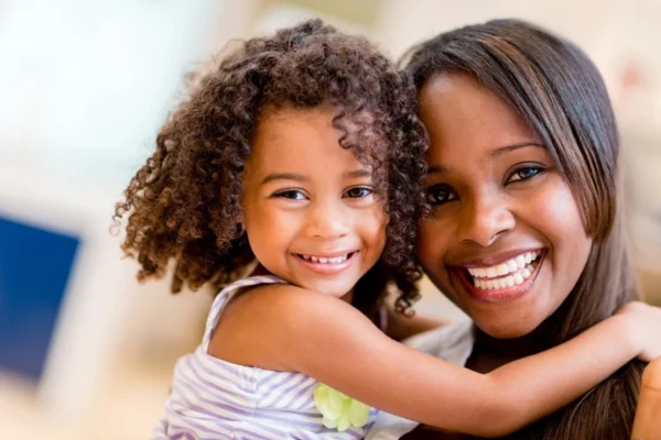 A joyful mother, a cardiologist, and her young daughter smiling brightly as they share an affectionate embrace.