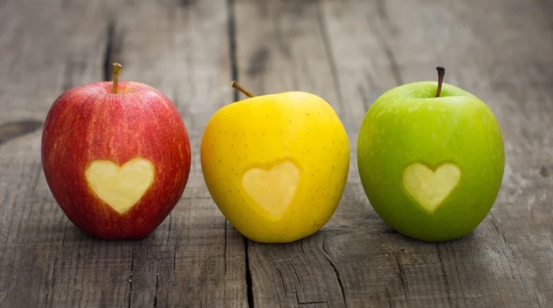 Three colorful apples with heart-shaped cutouts on a wooden surface representing cardiology.