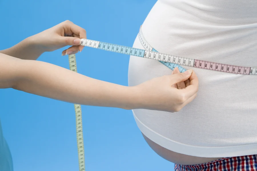 Measuring waist circumference against a blue background for cardiology assessment.