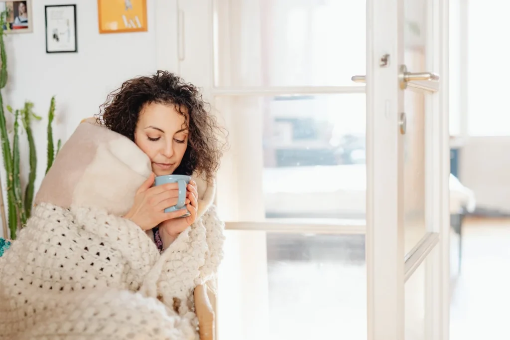 A person wrapped in a cozy blanket holding a warm cup, enjoying a peaceful moment by a sunny window, embodying the essence of heart health.