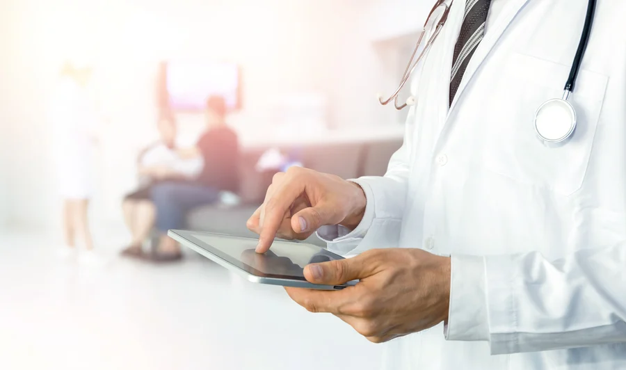 A cardiologist using a tablet computer with patients waiting in the background of a well-lit clinic setting at the Cardiovascular Institute of the South.