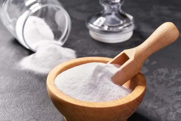 A wooden bowl filled with fine white salt with a scoop resting on top, and a salt shaker spilled over in the background on a dark textured surface, reminding one of the importance of moderation as advised