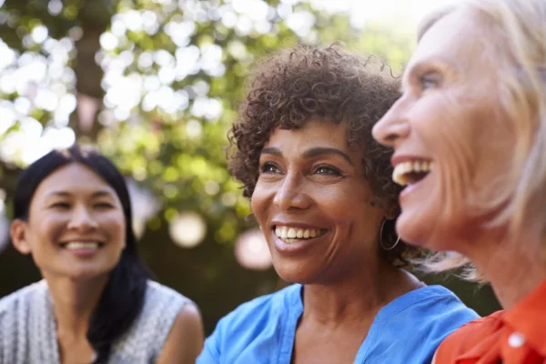 Three women of diverse backgrounds sharing a joyful moment under the shade on a sunny day, celebrating their successful recovery journeys at the Cardiovascular Institute of the South.